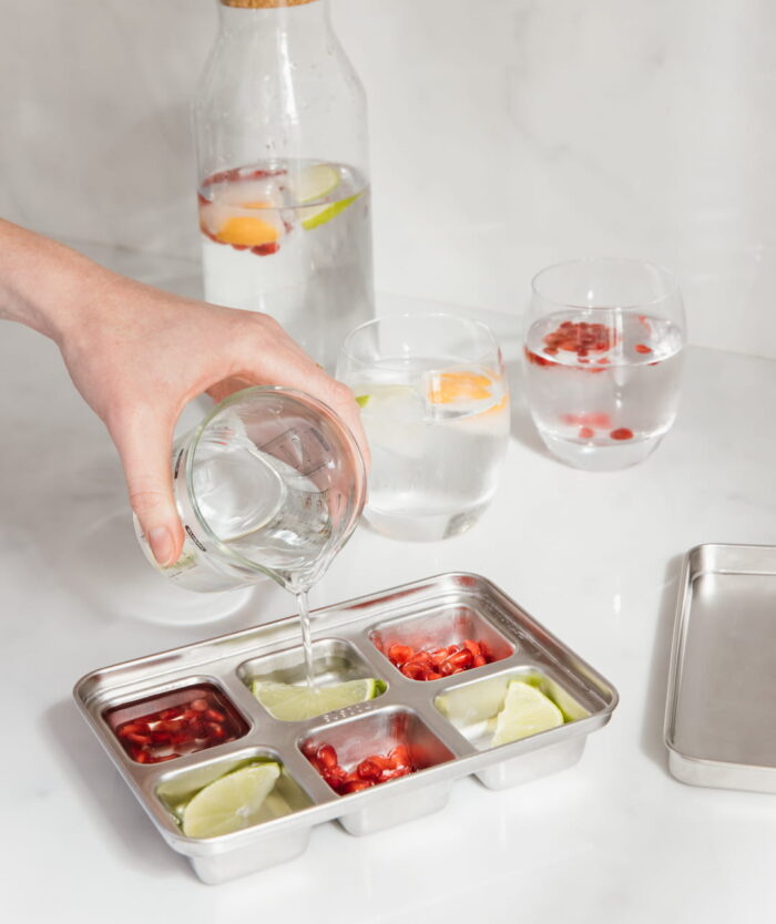 Eau versée dans Les Carrés Givrés de Casavida garnis de fruits pour faire des glaçons aromatisés