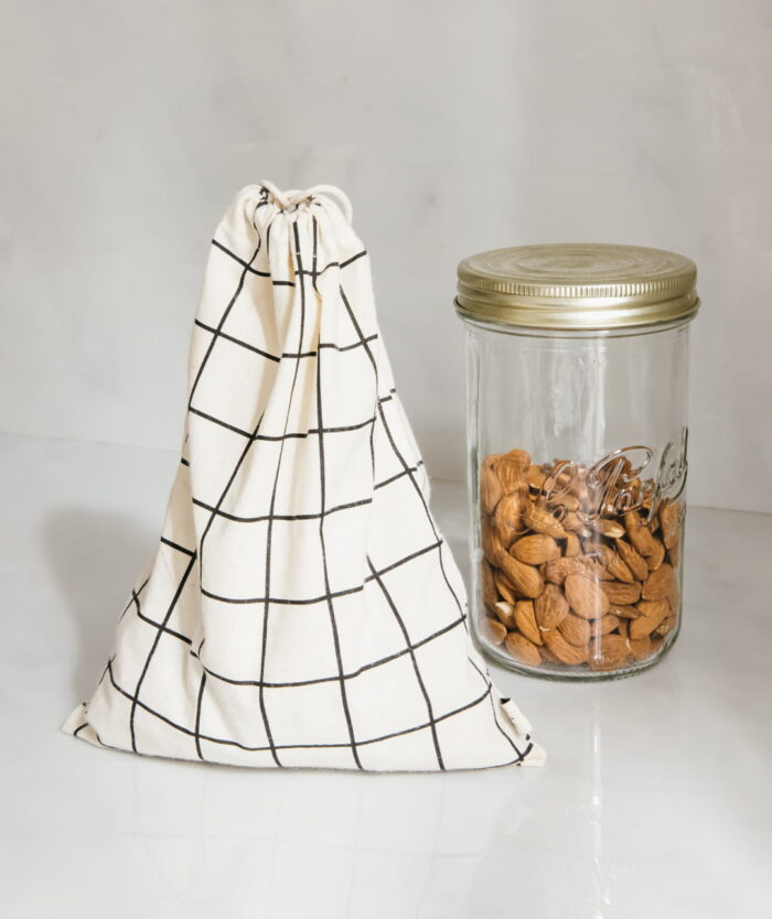 Les Sacs de Vrac de Casavida, sac à vrac réutilisable en coton à carreaux à côté d'un bocal d'amandes