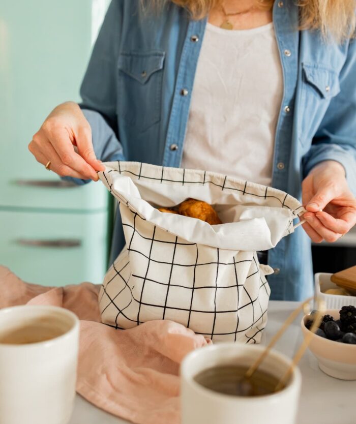 Femme ouvrant La Sache à Pains de Casavida remplie de viennoiseries, sac à pain réutilisable en coton à carreaux