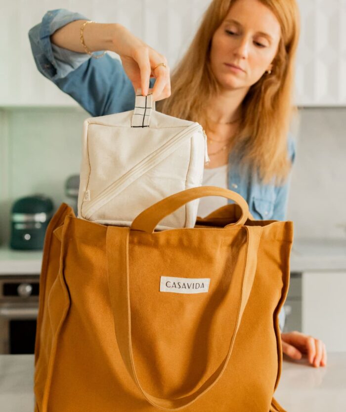 Femme glissant Le Vanity Cool de Casavida dans L'Irremplaçable Cabas Caramel de Casavida