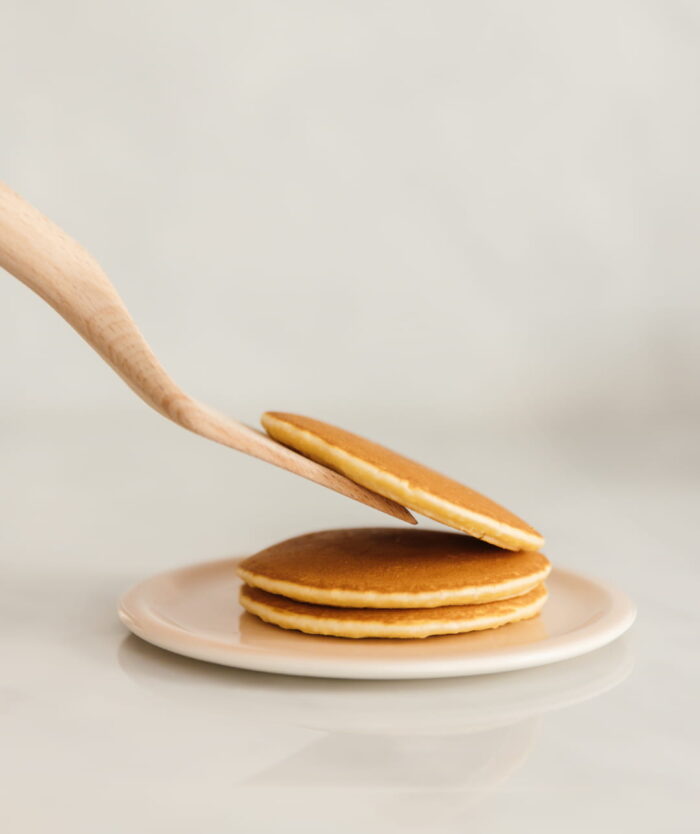 Pancakes empilés sur une assiette avec La Palette Coudée de Casavida, spatule en bois de hêtre