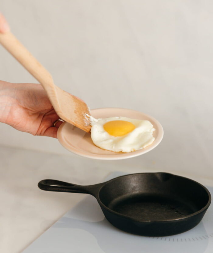 Œuf au plat glissé dans une assiette avec La Palette Coudée de Casavida, spatule en bois