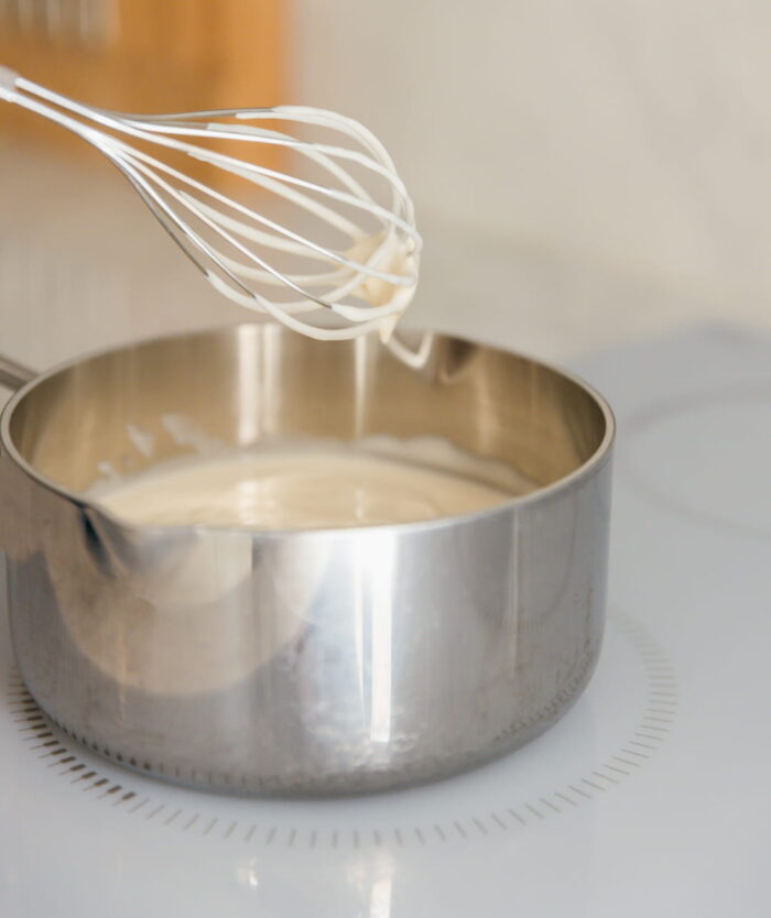 Le Fouet Énergique de Casavida au-dessus d'une casserole de béchamel, fouet inox à fils rigides