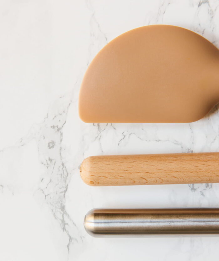 Détail de la tête en silicone et du manche de La Maryse Consciencieuse de Casavida à côté d'ustensiles en bois et inox