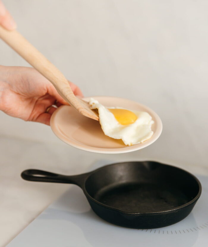 La Palette Coudée de Casavida servant un œuf au plat dans une assiette, spatule en bois de hêtre