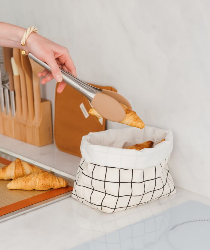 La Pince Agile de Casavida plaçant une viennoiserie dans une corbeille à pain en tissu à carreaux