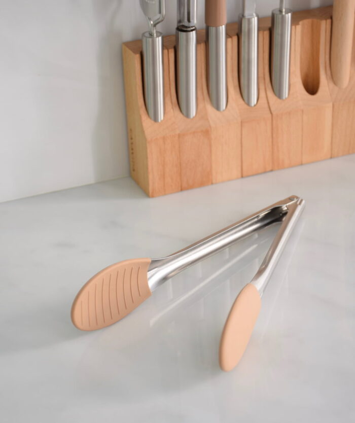 La Pince Agile de Casavida, pince de cuisine en inox et silicone, devant un socle d'ustensiles en bois