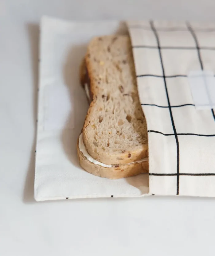 L'Enveloppe à Encas de Casavida ouverte avec un sandwich, pochette à snacks réutilisable en coton à carreaux