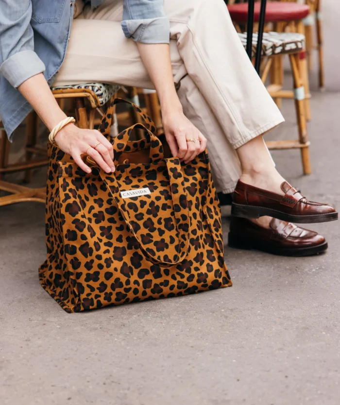 Femme assise avec L'Irremplaçable Cabas Léopard Moka de Casavida, sac cabas en coton bio, posé à ses pieds
